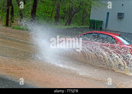 Une voiture rouge par les éclaboussures d'eau dangereusement élevé de conduire sur une route de l'inondation de la rivière en tant qu'il Banque D'Images