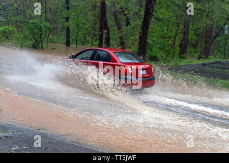 Une voiture rouge par les éclaboussures d'eau dangereusement élevé de conduire sur une route de l'inondation de la rivière en tant qu'il Banque D'Images