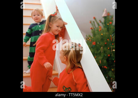 Trois jeunes enfants vêtus de pyjamas à à leur arbre de Noël le matin de Noël Banque D'Images