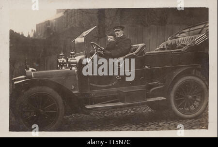 Vintage Edwardian Carte postale photographique d'un chauffeur britannique, jeune garçon de l'école et un chat Équitation dans une voiture classique. Prise en décembre 1909. Banque D'Images