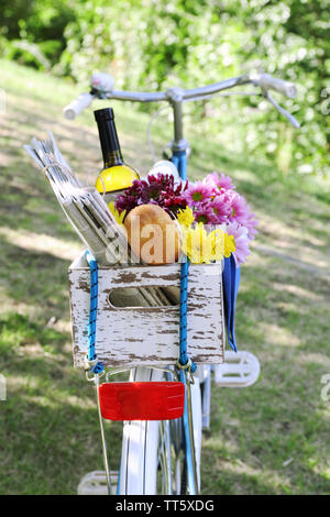 Location avec des fleurs, du pain et une bouteille de vin dans la boîte en bois sur fond d'herbe Banque D'Images