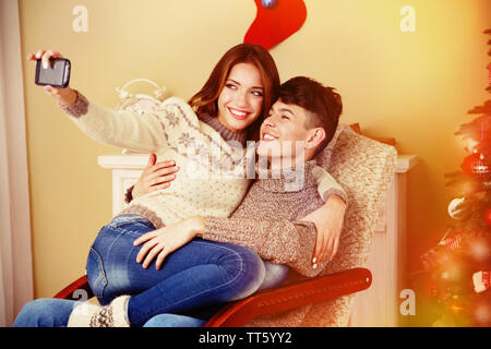 Jeune couple avec un téléphone mobile assis dans un rocking-chair près de l'arbre de Noël Banque D'Images