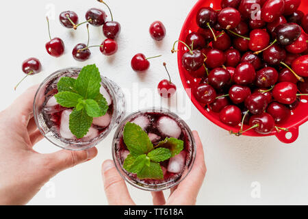 Le jus de cerise fraîche dans un verre avec les feuilles de menthe et de glace Close Up sur fond blanc, la femme part Banque D'Images