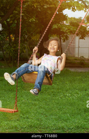 Asian kid en aire de accrocher sur des balançoires en arrière-plan lumineux ensoleillé jour Banque D'Images