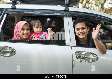 Jeune famille musulmane , transports, loisirs, road trip et personnes Concept - vue latérale d'homme heureux, femme et little girl waving at camera prêt à trav Banque D'Images