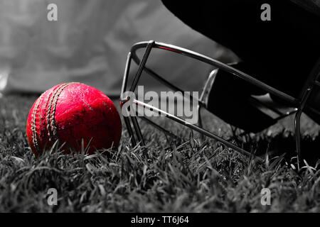 Balle de cricket rose avec halmet sur l'herbe verte. Photo en noir et blanc. Banque D'Images