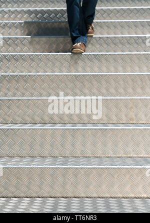 Les jambes d'une femme vêtu de jeans et portant des brown montre marchant dans la lumière vive l'aluminium d'escalier Banque D'Images