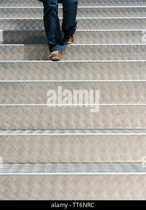 Les jambes d'une femme vêtu de jeans et portant des brown montre marchant dans la lumière vive l'aluminium d'escalier Banque D'Images