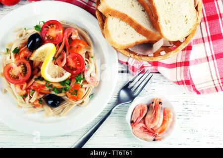 Pâtes aux crevettes, olives noires et de la sauce tomate sur la plaque sur fond de bois Banque D'Images