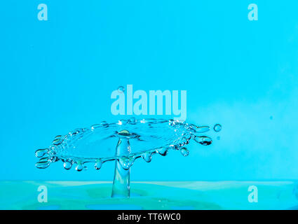 Goutte d'eau tombant et ayant des répercussions sur un plan d'eau après avoir atteint la surface et la formation de gouttelettes d'eau différentes sur un fond bleu. Banque D'Images