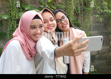 trois femmes asiatiques et musulmanes emportant un selfie avec un smartphone au parc extérieur Banque D'Images