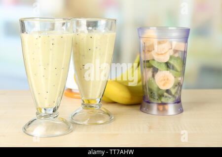 Lunettes avec milkshake et les tranches de fruits dans un bol de blender sur table en bois, sur fond lumineux Banque D'Images