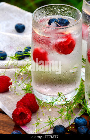 Les framboises et les bleuets dans un verre avec de la glace sur la table dans la nature Banque D'Images