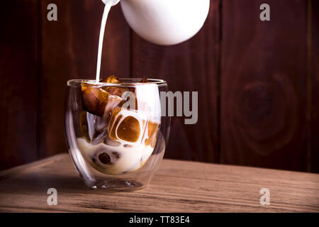 Le lait est versé dans les cubes de café glacé dans un bécher en verre double-moderne. Banque D'Images