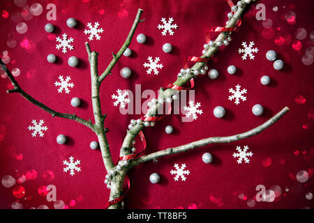 Concept d'arbre de Noël avec des branches d'arbres sans feuilles, flocons de neige, les globules de paillettes, ruban rouge et la chaîne de perles sur fond rouge avec bokeh Banque D'Images