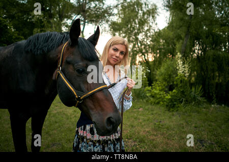 Fille sur la pelouse au coucher du soleil avec un cheval brun Banque D'Images