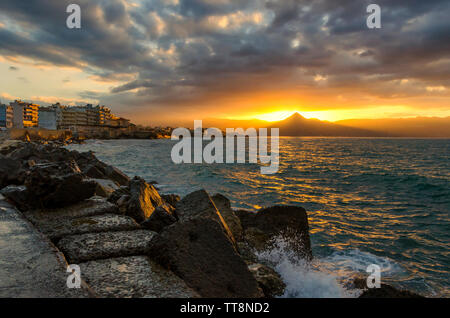 Héraklion, Crète - Grèce. De soleil colorés avec ciel nuageux sur la mer et la ville d'Héraklion. Soleil se reflète sur la mer et les rochers Banque D'Images