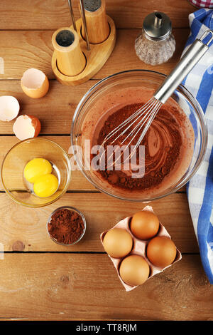 Préparation de la crème avec les oeufs et le cacao dans un bol de verre sur fond de bois Banque D'Images