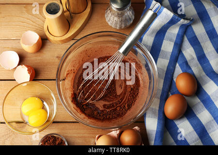 Préparation de la crème avec les oeufs et le cacao dans un bol de verre sur fond de bois Banque D'Images