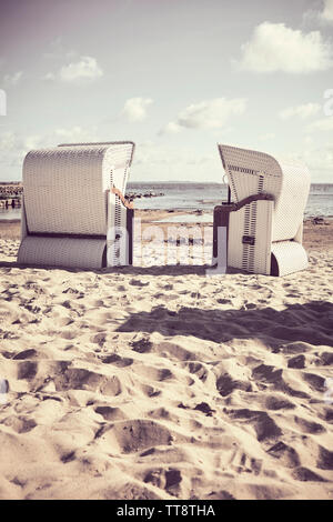 Retro photo stylisée de deux chaises de plage en osier vide sur une plage. Banque D'Images