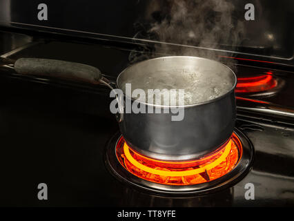 Coup horizontal d'une casserole d'eau bouillante sur une plaque de cuisson avec un élément rouge lumineux avec copie espace. Banque D'Images