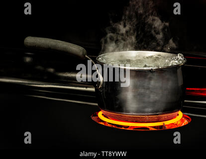 Coup horizontal d'une casserole d'eau bouillante sur une plaque de cuisson avec un élément rouge lumineux. Banque D'Images