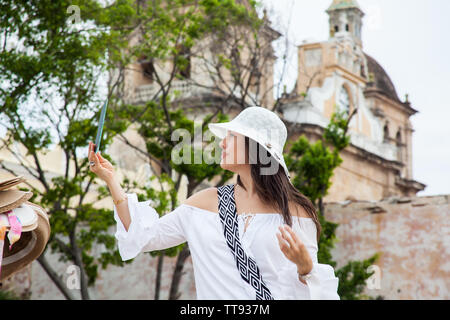 Belle jeune femme essayant des chapeaux d'en acheter un à partir d'un vendeur de rue dans la ville fortifiée de Cartagena de Indias Banque D'Images