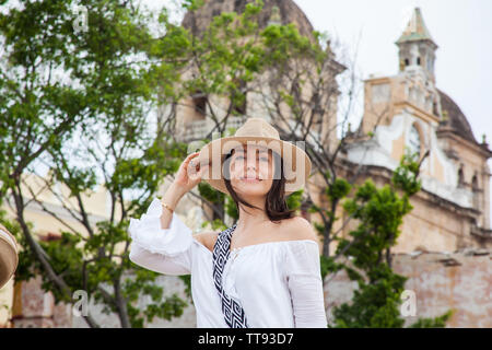 Belle jeune femme essayant des chapeaux d'en acheter un à partir d'un vendeur de rue dans la ville fortifiée de Cartagena de Indias Banque D'Images