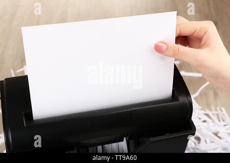 La destruction de main de femme feuille de papier avec shredder sur table en bois, gros plan Banque D'Images