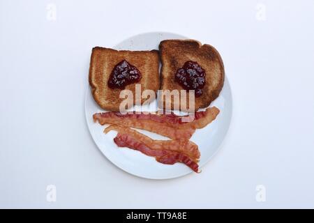 Smiley Petit déjeuner de pain grillé et de bacon sur une plaque blanche sur un fond blanc. Banque D'Images