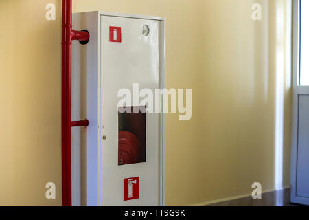 Armoire métallique blanche avec enrouleur de tuyau d'extinction d'incendie sur le mur de lumière de fond de l'espace de copie. Banque D'Images