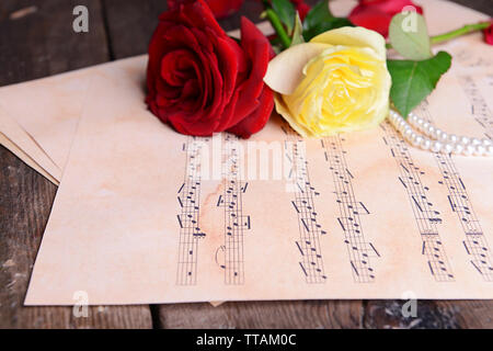 Belles roses avec des perles sur les feuilles de musique sur table en bois, gros plan Banque D'Images