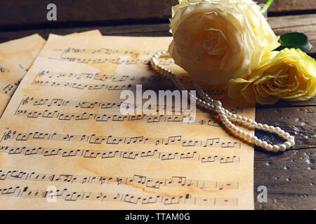 Belles roses avec des perles sur les feuilles de musique sur table en bois, gros plan Banque D'Images