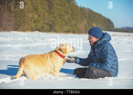 Un humain et le chien sont les meilleurs amis. L'homme avec le chien assis dans un champ neigeux en hiver. Formés Labrador retriever dog étend la patte de l'homme Banque D'Images