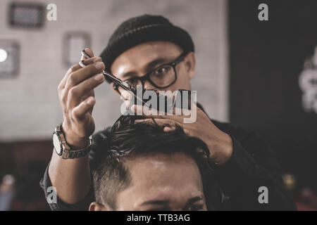 Portrait de coiffure professionnel faire couper les cheveux de son homme séduisant client avec ciseaux et peigne en vintage barbershop Banque D'Images