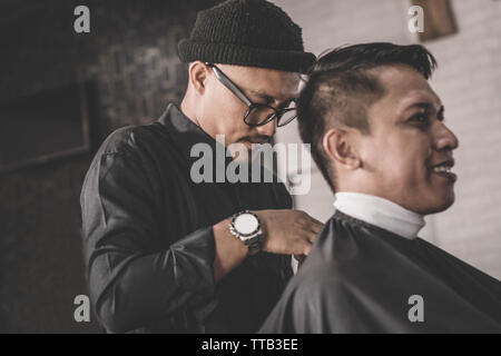 Close up portrait of coiffure coiffure cheveux un client qui assis dans un fauteuil avec la main et pommade dans salon de barbier ou Banque D'Images