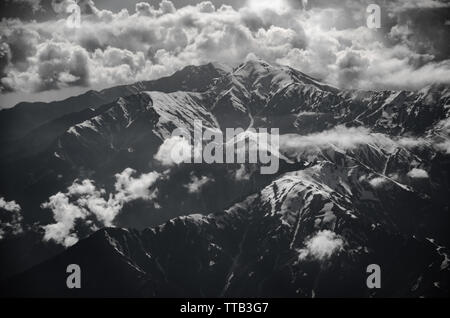 Photographie en noir et blanc d'des envoûtantes montagnes de l'himalaya culminant à travers les nuages sur un jour nuageux du vol de Delhi à Srinagar. Banque D'Images