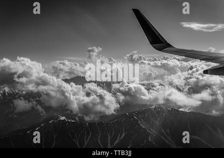 Photographie en noir et blanc d'des envoûtantes montagnes de l'himalaya culminant à travers les nuages sur un jour nuageux du vol de Delhi à Srinagar. Banque D'Images