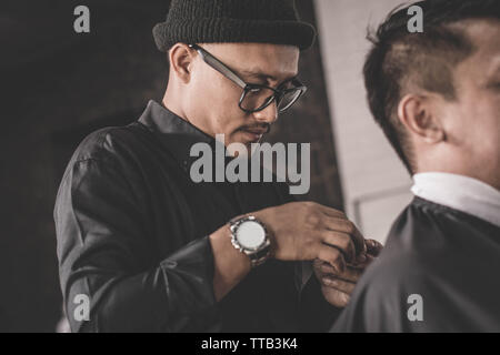 Close up portrait of coiffure coiffure cheveux un client qui assis dans un fauteuil avec la main et pommade dans salon de barbier ou Banque D'Images