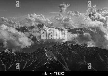 Photographie en noir et blanc d'des envoûtantes montagnes de l'himalaya culminant à travers les nuages sur un jour nuageux du vol de Delhi à Srinagar. Banque D'Images