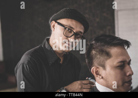 Close up portrait of coiffure coiffure cheveux un client qui assis dans un fauteuil avec la main et pommade dans salon de barbier ou Banque D'Images