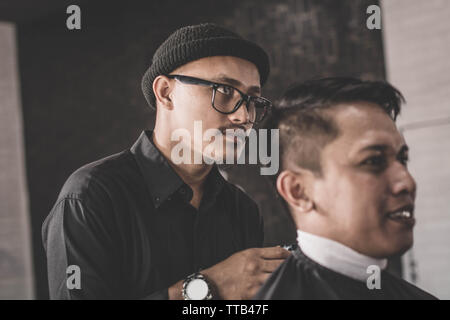 Close up portrait of coiffure coiffure cheveux un client qui assis dans un fauteuil avec la main et pommade dans salon de barbier ou Banque D'Images