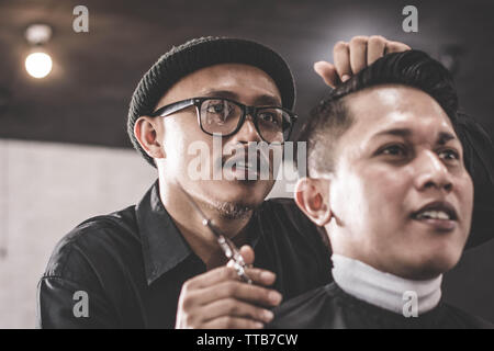 Close up portrait of coiffure coiffure cheveux coiffage des cheveux de son client qui assis dans un fauteuil avec la pommade et le peigne dans la main ou au salon de coiffure Banque D'Images