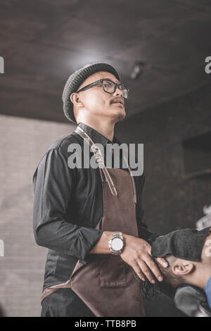 Portrait de coiffure homme massage à la clientèle avec des serviettes qui vous détendre assis au fauteuil de barbier Banque D'Images