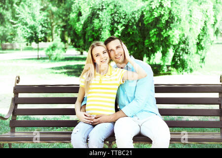 Jeune femme enceinte avec mari assis sur un banc dans le parc Banque D'Images