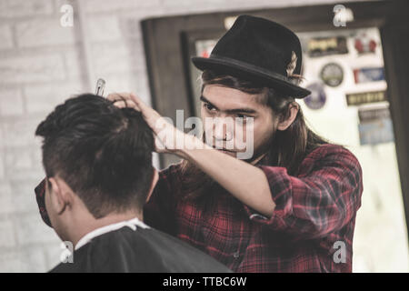 Portrait de l'homme asiatique professionnel avec de longs cheveux bruns travail en tant que client avec sa coupe coiffure ciseaux et peigne en coiffure Banque D'Images
