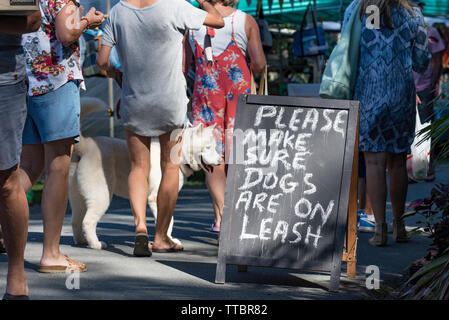 Personnes et un chien à l'agriculteur d'un week-end au marché communautaire Pacific Palms, Nouvelle Galles du Sud avec un signe lui demandant de garder leurs propriétaires de chien en laisse. Banque D'Images