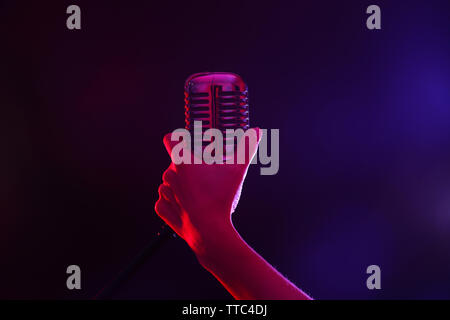 La tenue d'une main de femme contre micro rétro arrière-plan coloré Banque D'Images