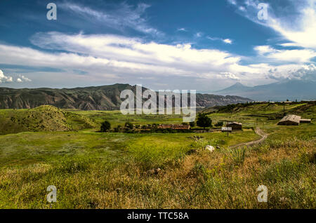 La route menant à la montagne surplombant le village de crêtes Gegham et la silhouette du mont Ararat Sur le fond bleu du ciel couvert de nuages Banque D'Images