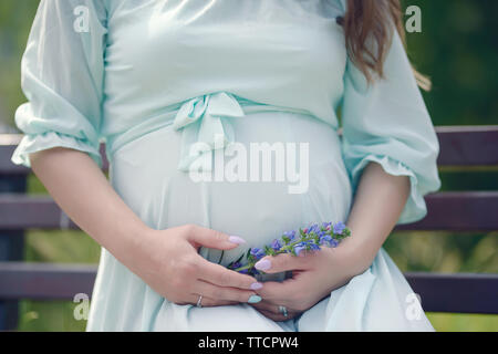 Close up of beautiful young woman dans son dernier trimestre de grossesse portant une robe d'été vaporeuse couleur menthe et holding Flowers Banque D'Images